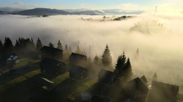Aerial view of a village houses on hill top in autumn foggy mountains at sunrise alt