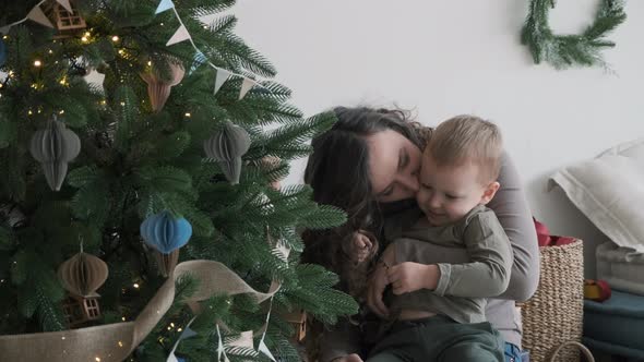 Woman Sitting with Little Son Near Christmas Tree alt