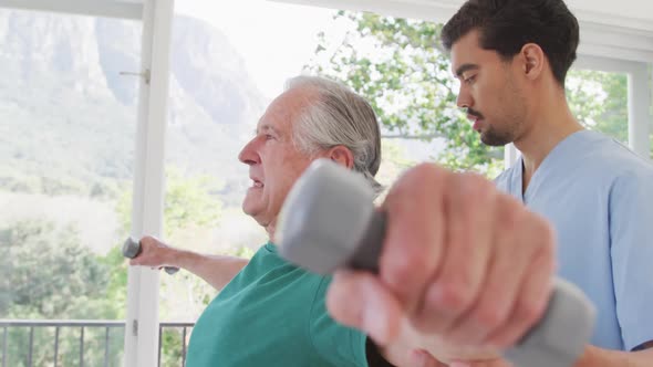 Male physiotherapist looking at senior man exercising with dumbbells in retirement home alt
