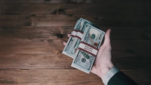 Male Hand Hold Three Stacks of 10000 US Dollar Bills on Wooden Background alt