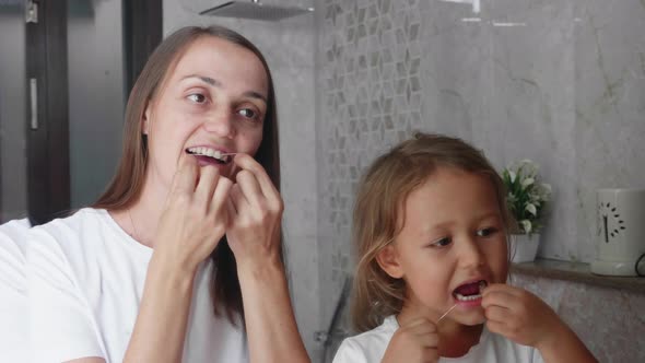 Mom and Little Daughter Brush Their Teeth with Dental Floss at Bathroom Together alt