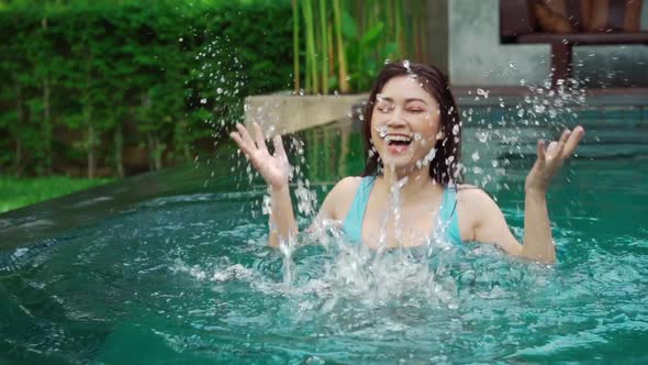 slow-motion of cheerful woman playing water splashing in the swimming pool alt