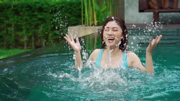 slow-motion of cheerful woman playing water splashing in the swimming pool