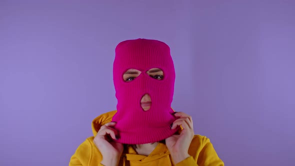 Close Up Young Woman Puts on Pink Balaclava on Purple Background alt