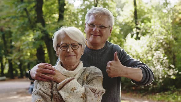 Happy Old Couple Hugging in Park. Senior Man Flirting with Elderly Woman. Thumbs Up alt
