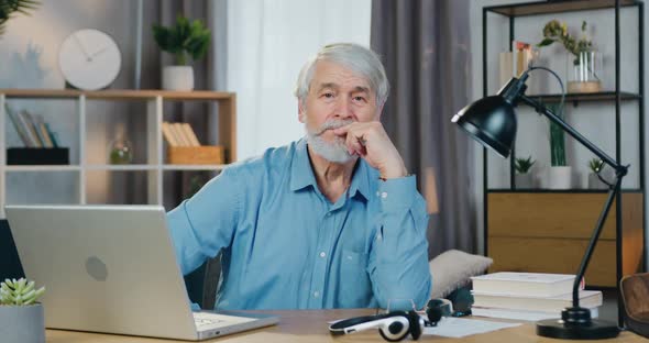 Old Man Sitting at Table with Laptop and Looking at Camera alt