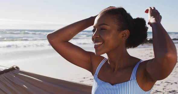 Close up of african american woman smiling while sitting on a hammock at the beach alt