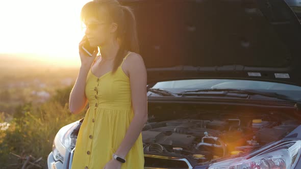 Stressed woman driver talking on a phone standing near her vehicle with popped hood  alt