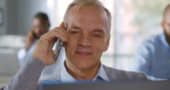 Close Up of Mature Businessman Talking on Mobile Phone Sitting at Office Desk alt