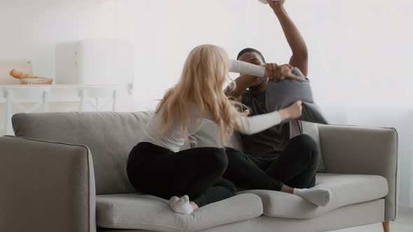 Happy Diverse Couple Having Pillow Fight On Sofa At Home alt