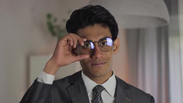 Indian businessman adjusts glasses and nods smiling behind camera, static alt