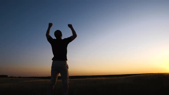 Happy man celebrating victory jumping and waving his hands against sunset background