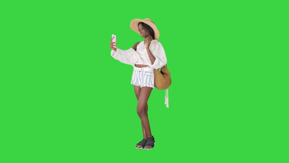 Smiling African American Woman Wearing Straw Hat and Taking Selfie on Smartphone on a Green Screen alt