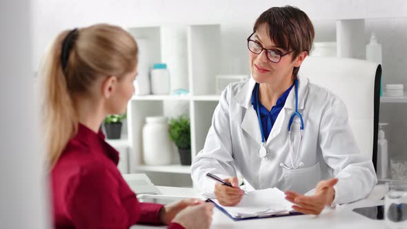 Smiling Female Medical Worker in White Coat Talking with Girl Patient at Hospital Medium Closeup alt