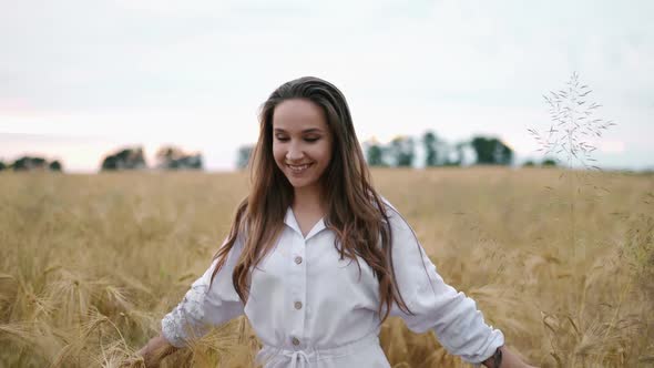 A Young Girl Happily Walking in Slow Motion Through a Field Touching with Hand Wheat Ears Beautiful