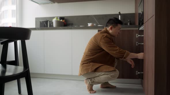 Confident Asian man wearing casual cloth taking things out of the washing machine alt