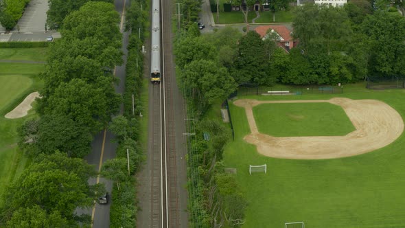Aerial View of a Train Passing Through Garden City and Near a Baseball Field alt