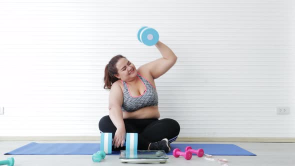 Stressed Asian overweight female doing workout with dumbbells in living room at home
