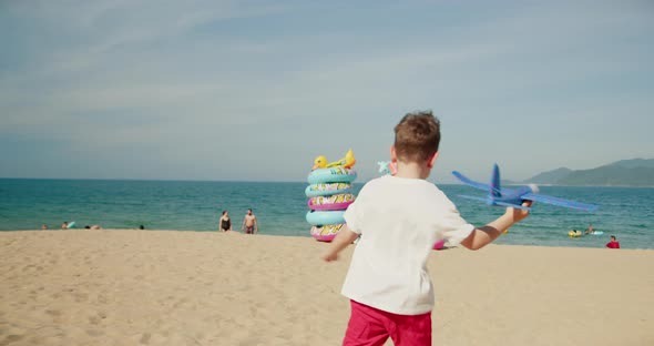 Happy Child Runs with a Toy Plane at Sunset Over the Beach Sand Towards Sea alt