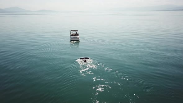 A wakeboarder is ready to start in the water, waiting for the boat to accelerate, aerial drone view, alt