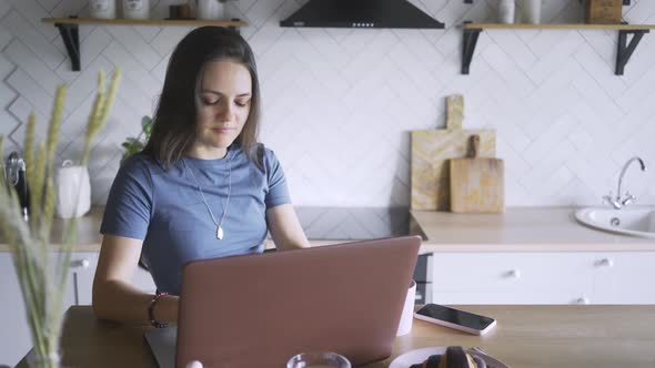 Woman Works on Laptop at Table in Brightly Lit Kitchen