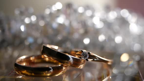 Three Beautiful Gold Rings a Diamond Engagement Ring and an Engagement Ring Lie Against a Glittering alt