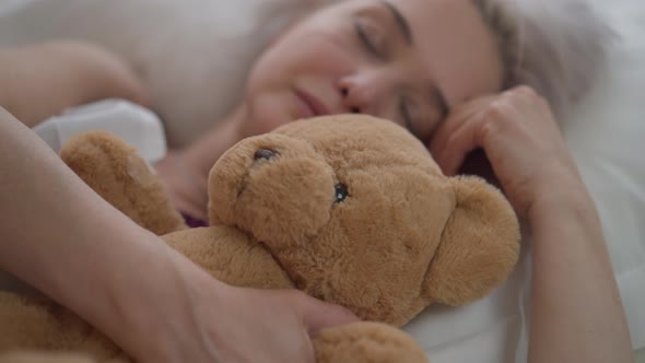 Closeup Teddy Bear with Blurred Mature Woman Sleeping in Bed at Background alt