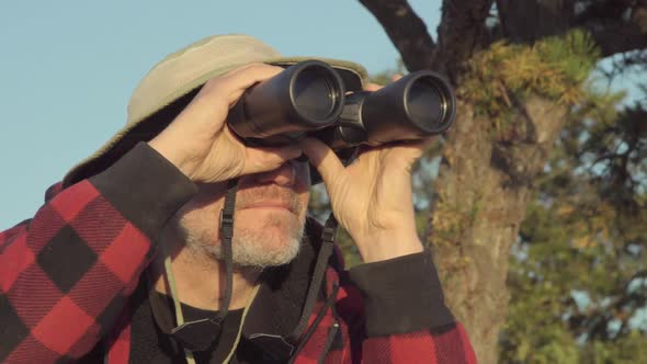 An older hiker looking through binoculars while on a scenic hike in the mountains alt