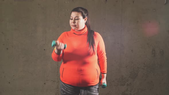 Young Plump Female Bodybuilder Is Training with Dumbbells alt