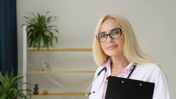 Happy Senior Woman Doctor Wearing White Medical Coat and Stethoscope Looking at Camera alt