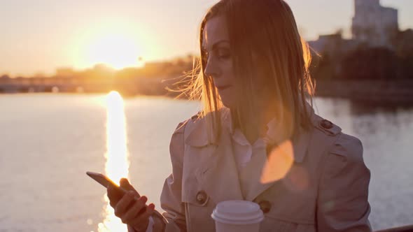 Woman Typing Message and Drinking Coffee at Sunset alt