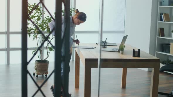 Woman Standing By the Table Massaging Back Suffering From Pain or Inflammation alt