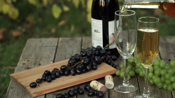 White Wine is Poured Into Glass on Wooden Table with Grapes at Summer Sunset Outdoors