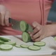 Close Up Of Asian Woman Holding A Knife And Slicing Cucumber On The Chopping Board In The Kitchen - VideoHive Item for Sale
