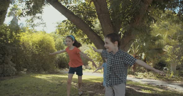 Three kids playing together outdoors on the grass, running around alt