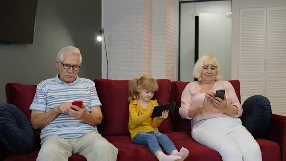 Grandparents and Grandchildren Sit on the Couch at Home and Use Mobile Phones and Digital Tablet alt