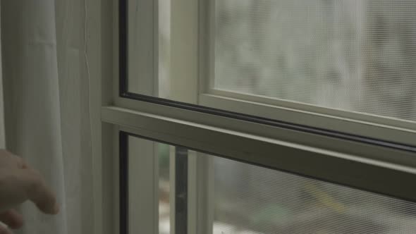 Hand covering a glass door or window with curtains alt