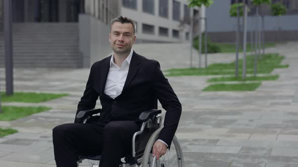 Handicapped Successful Businessman in Classical Suit Riding While Sitting in Wheelchair at Street