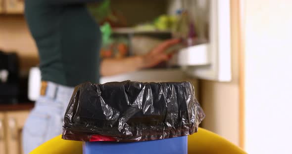 Woman throws in the trash uneaten spoiled products fruits, glasses, from the fridge alt