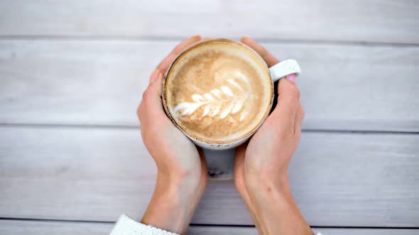 Female Hands Taking Cup of Hot Cappuccino with Latte Art From Table alt