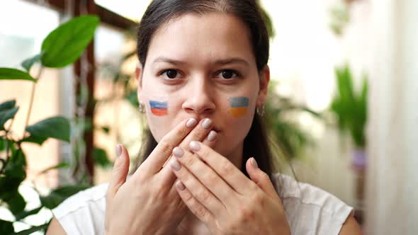 Young RussianUkrainian Girl with the Flag of Ukraine and Russia on Her Face is Closing Mouth alt