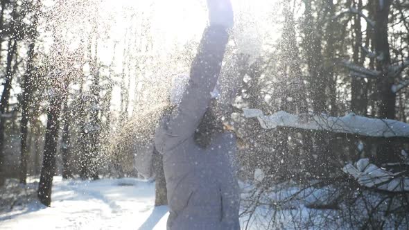 Young Happy Woman in Winter Clothes Throwing Handful of Snow and Enjoying Falling Snowflakes alt