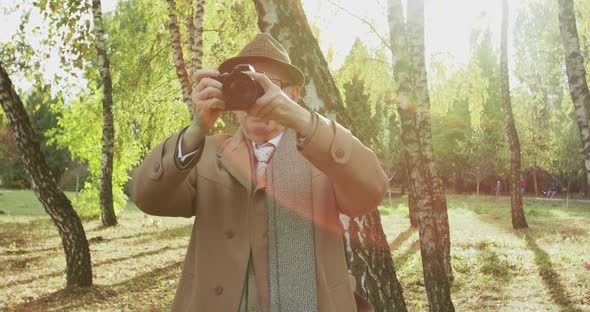 Old Photographer Taking Pictures on Camera in Sunny Park alt