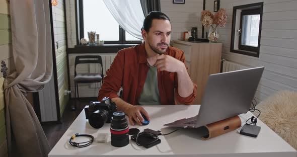 A Young Handsome Male Photographer and Videographer Works at Home on a Laptop alt