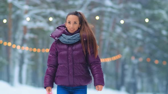 Smiling Girl in Jacket and Scarf Jumps on Skates on Ice Rink