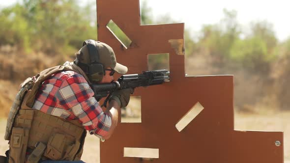 Caucasian Man in Headphones Sunglasses Reloading Airsoft Gun Sitting Behind Cover Position alt