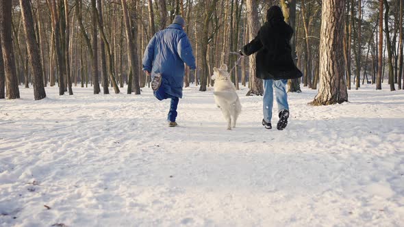 Happy Family Runs Through the Winter Snowy Forest with a Dog alt