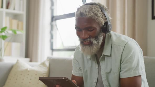 Video of african american senior man using tablet and headphones alt