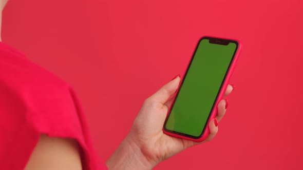 Female Hand Holds Mobile Phone with Green Workspace Mock Up Screen on Red Studio Background in alt