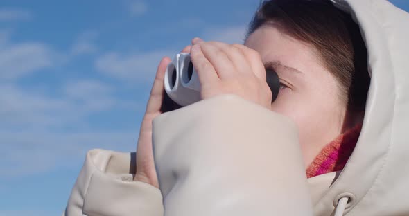 Happy Young Woman Looking Through Binoculars on Background of the Sky Closeup